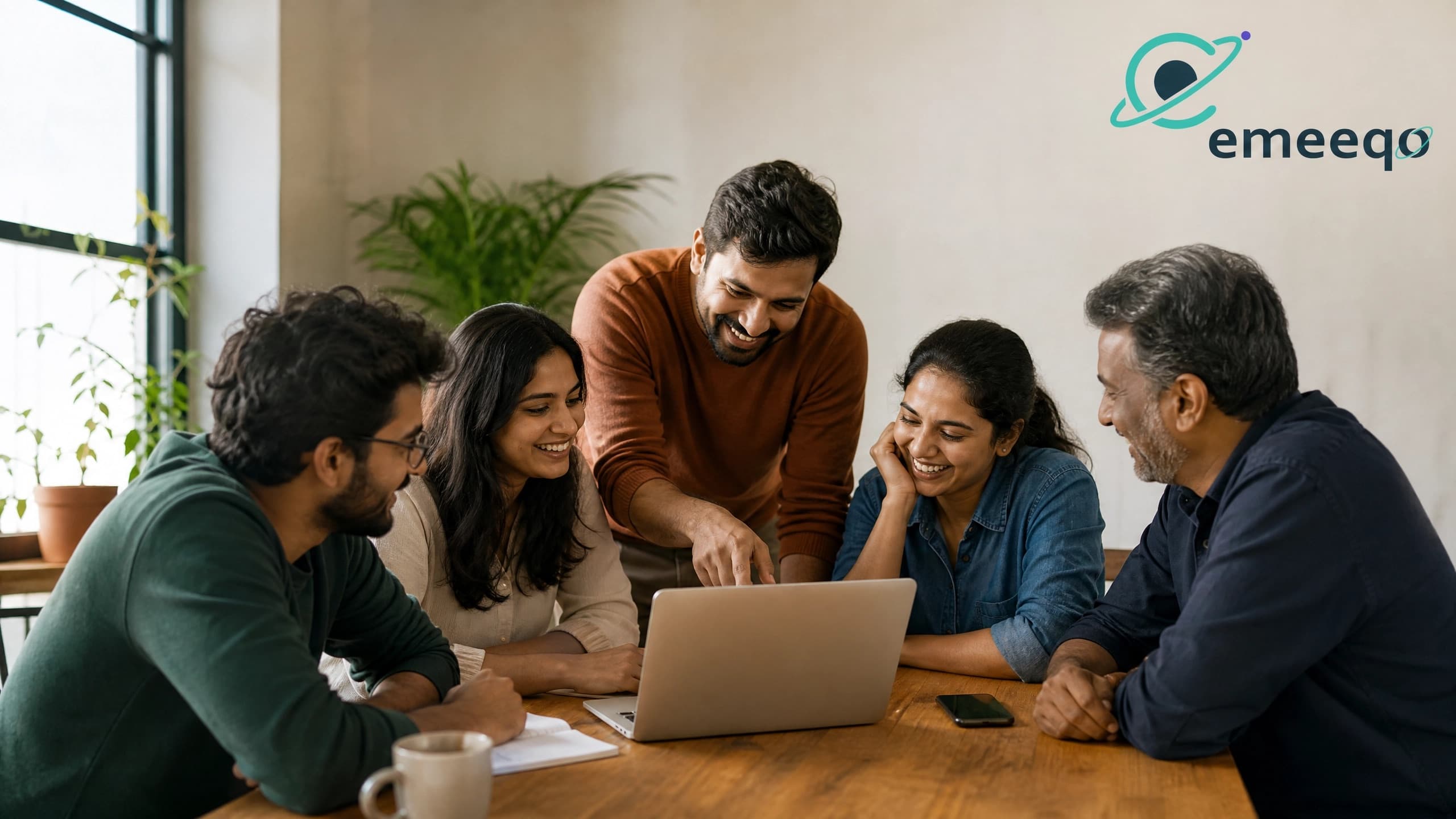 The emeeqo team collaborating around a laptop in a bright office
